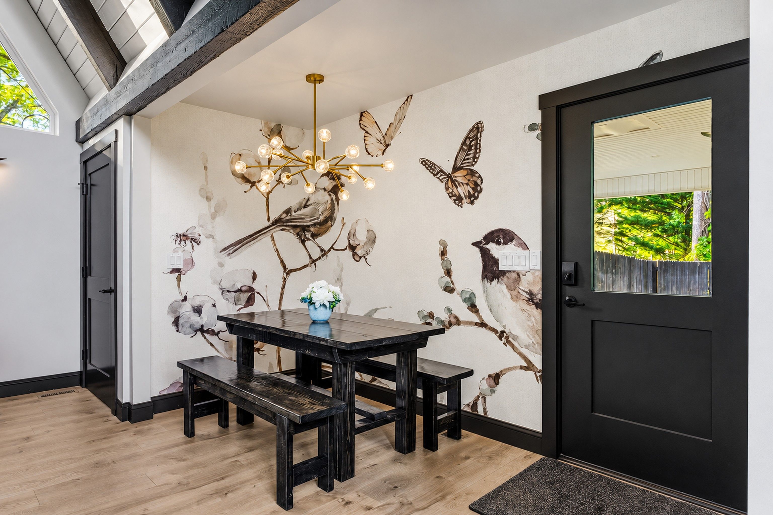 A dining area with a table and benches, a chandelier, and wall art featuring birds and flowers.