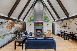A spacious loft with a high ceiling, a fireplace, and a large painting of a landscape. - River Views | A-Frame + Hot Tub + Fenced Yard + Adventure Fort + Fire Pit (Mount Airy)