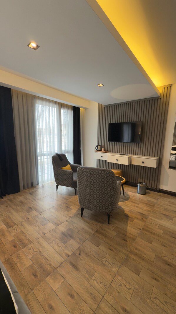 Una sala de estar moderna con piso de madera, dos sillones estampados, una mesita y un televisor de pantalla plana montado en la pared, con una lámpara en el techo.