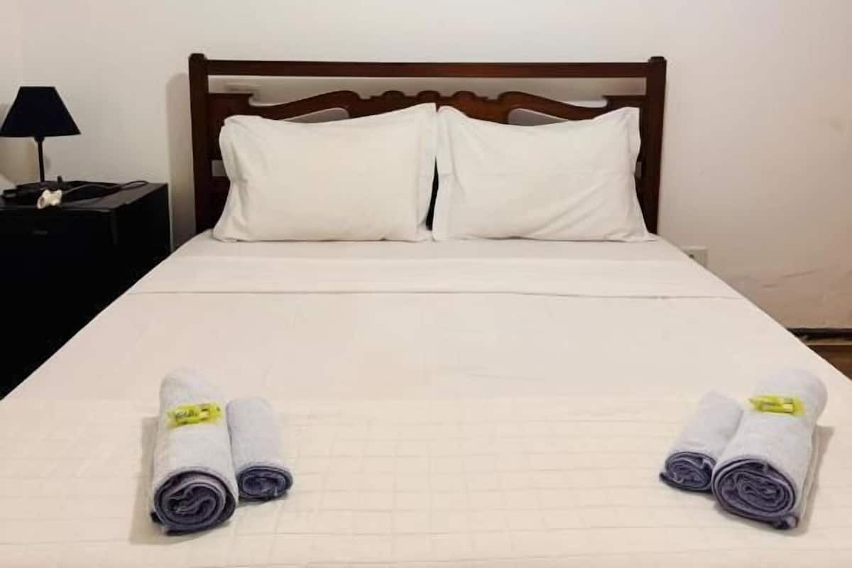 A neatly made bed with a wooden headboard, white pillows, and rolled towels on the bed.