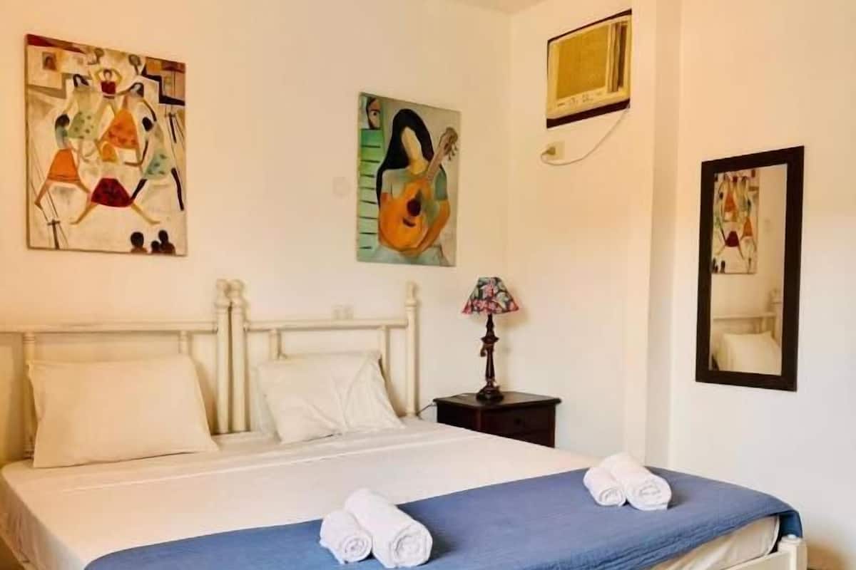 A hotel room with a bed, white walls, and two paintings.