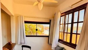 Une pièce de taille modeste, dotée d’un ventilateur de plafond, d’une fenêtre avec des rideaux, d’un canapé et d’une petite table avec des chaises.