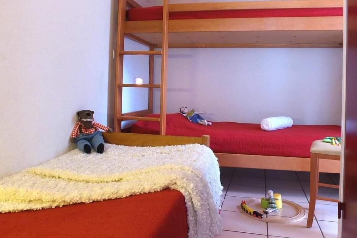 A bunk bed room with a toy bear on the lower bunk, a small table with toys, and a white blanket on the floor.