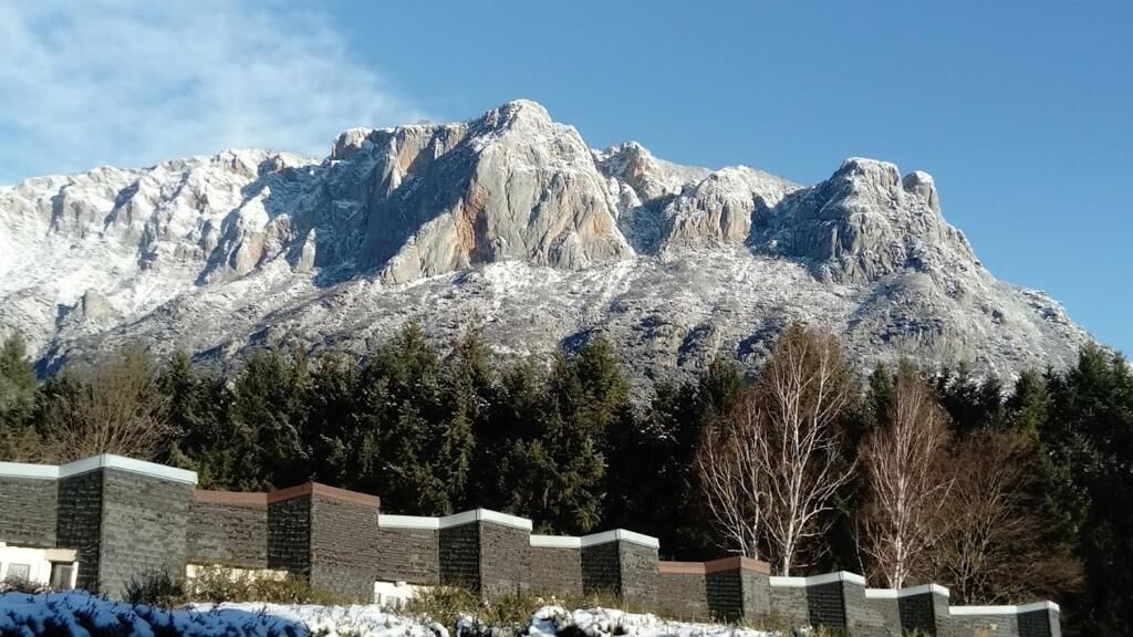 A mountain range with snow-covered peaks and a stone wall in the foreground.