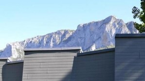 Een modern gebouw met een patio, uitgerust met witte plastic stoelen en een tafel, omgeven door groen en uitzicht op een berg.