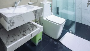 A modern bathroom with a marble sink, a toilet, a glass shower enclosure, and a large mirror. - Lankahuts (Negombo)