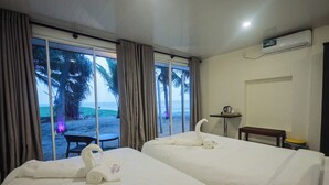 A hotel room with two beds, a small table, a bench, and a view of the beach. - Lankahuts (Negombo)