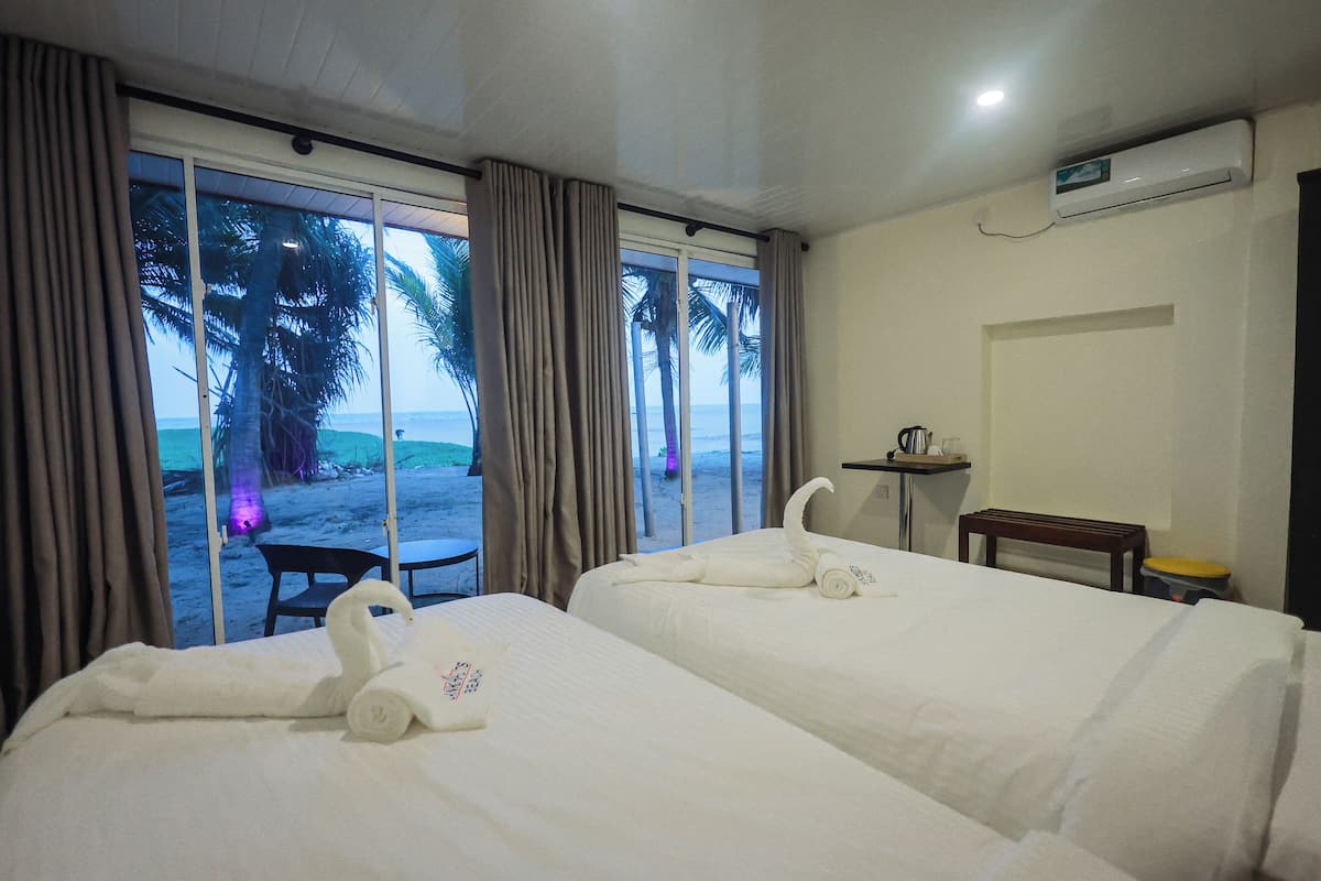 A hotel room with two beds, a small table, a bench, and a view of the beach.