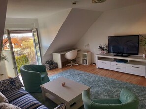 Un salon moderne avec un téléviseur, un canapé et des fauteuils verts.