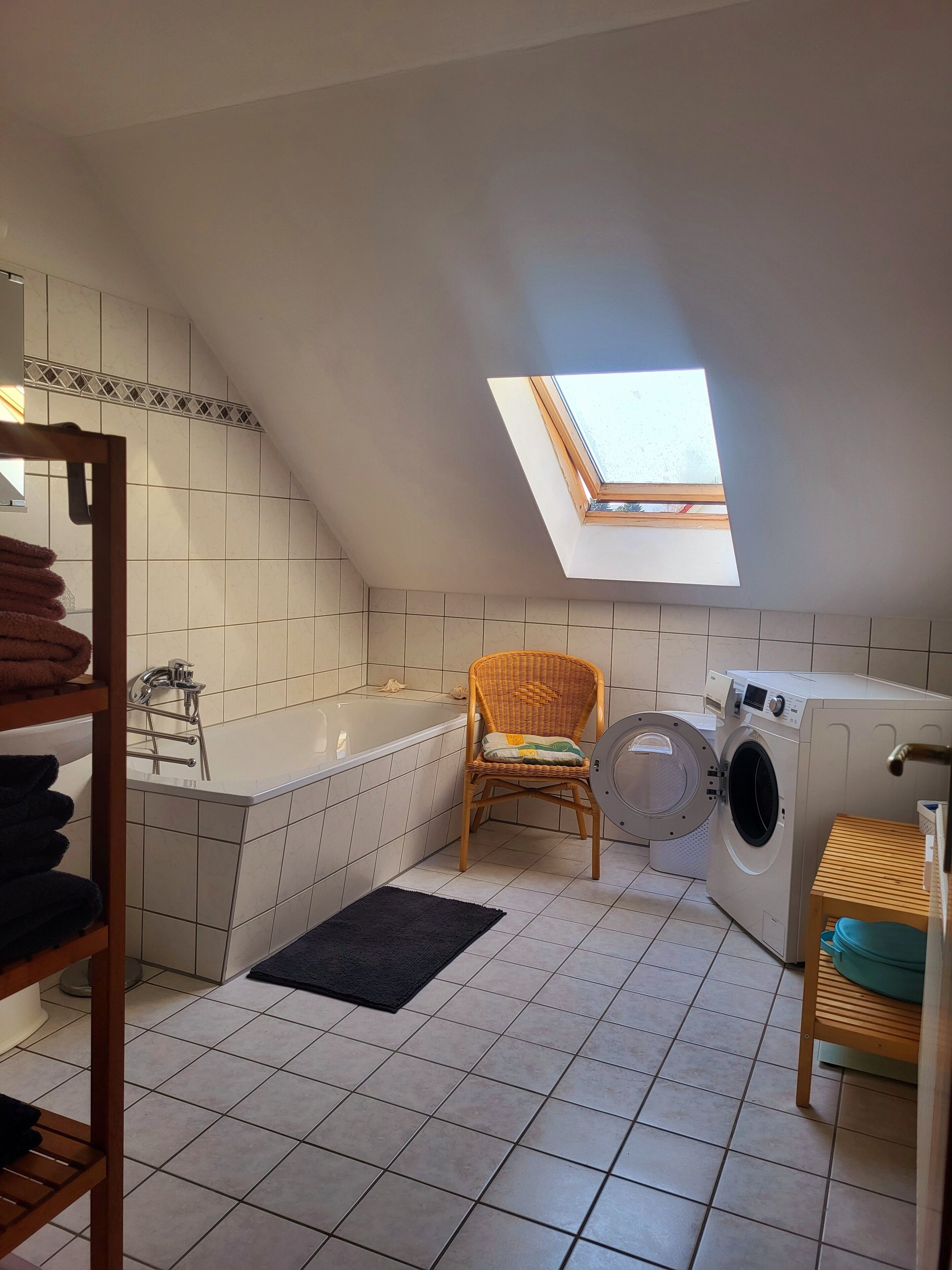 Une petite buanderie bien éclairée, dotée d’un puits de lumière, d’un lave-linge, d’une chaise et d’une baignoire.