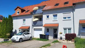 Ein zweistöckiges Wohngebäude mit einem Auto auf der Auffahrt, einem roten 'P' auf dem Boden und einem strahlend blauen Himmel.