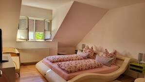 Ein Schlafzimmer mit einem gebogenen Bett, einem Schreibtisch, einem Stuhl, einem Heizkörper und einem Fenster mit Jalousien.