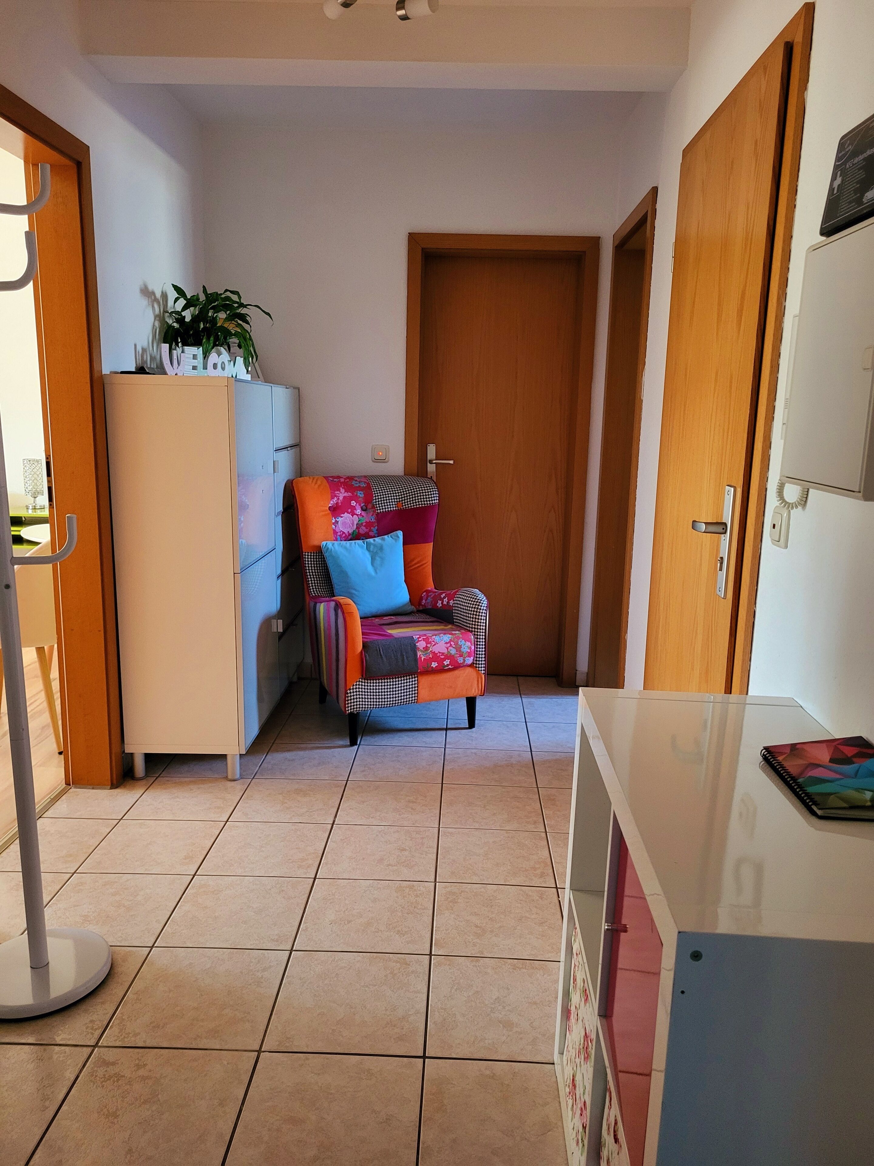 Un espace de vie compact comprenant un coin cuisine, une chaise colorée, un meuble blanc et une porte en bois.