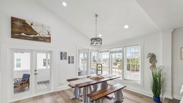 Un vaste espace dédié à la salle à manger, avec une grande table en bois et des bancs, de grandes fenêtres équipées de stores et un luminaire suspendu.