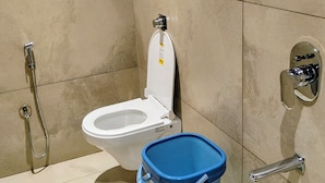 A modern bathroom with a toilet, a shower, and a blue trash bin. - Kubo by Convivial Hotels (Raipur)