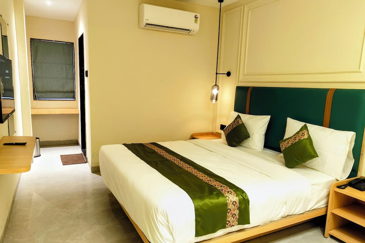 A hotel room with a bed, bedside table, and an air conditioning unit on the wall.