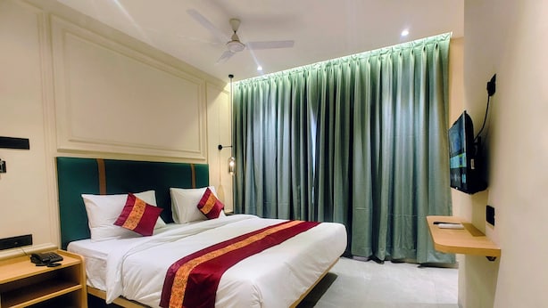 A hotel room with a bed, bedside table, and a TV mounted on the wall. - Kubo by Convivial Hotels (Raipur)