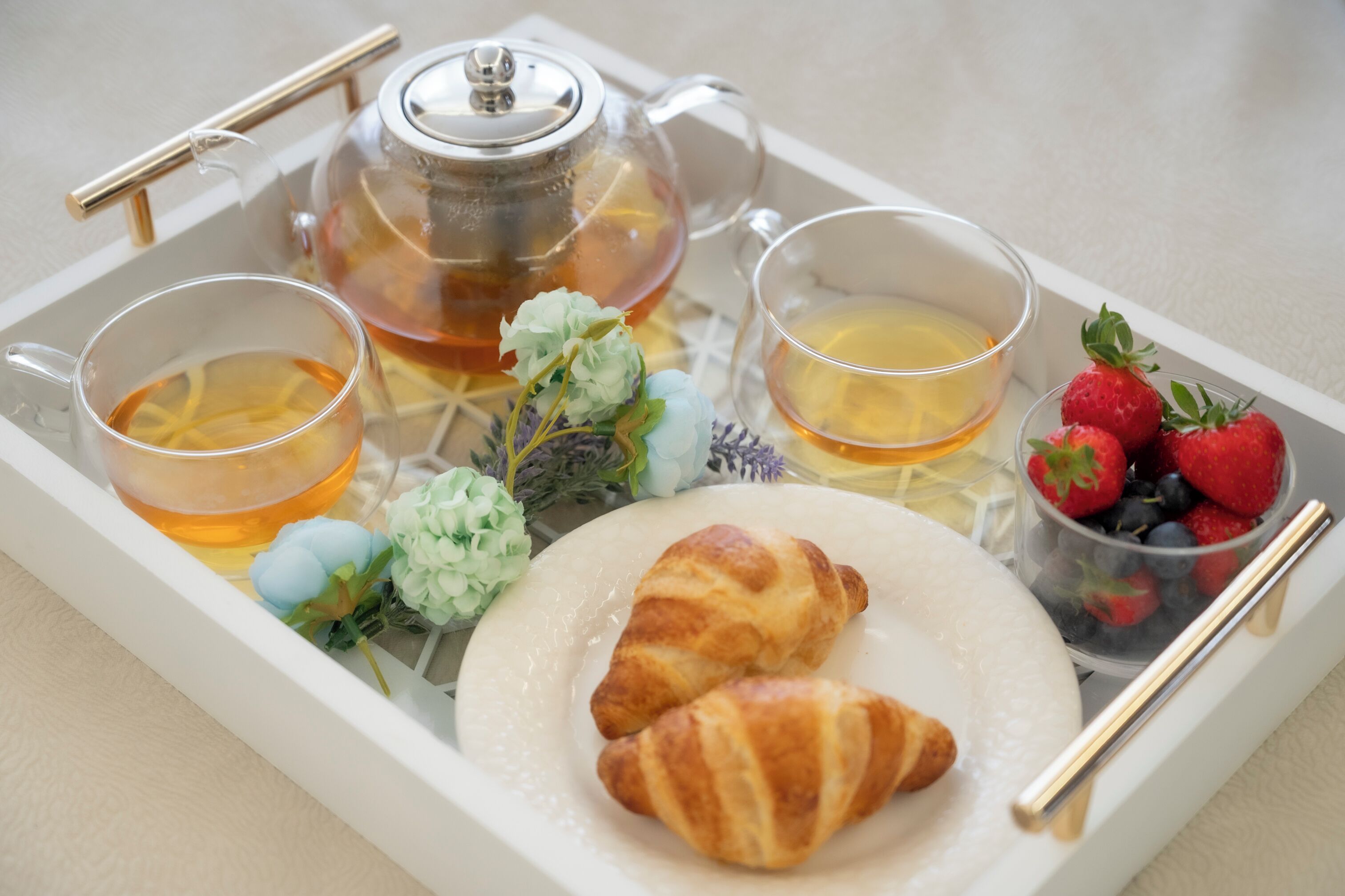 A tray with tea, croissants, strawberries, and a teapot.