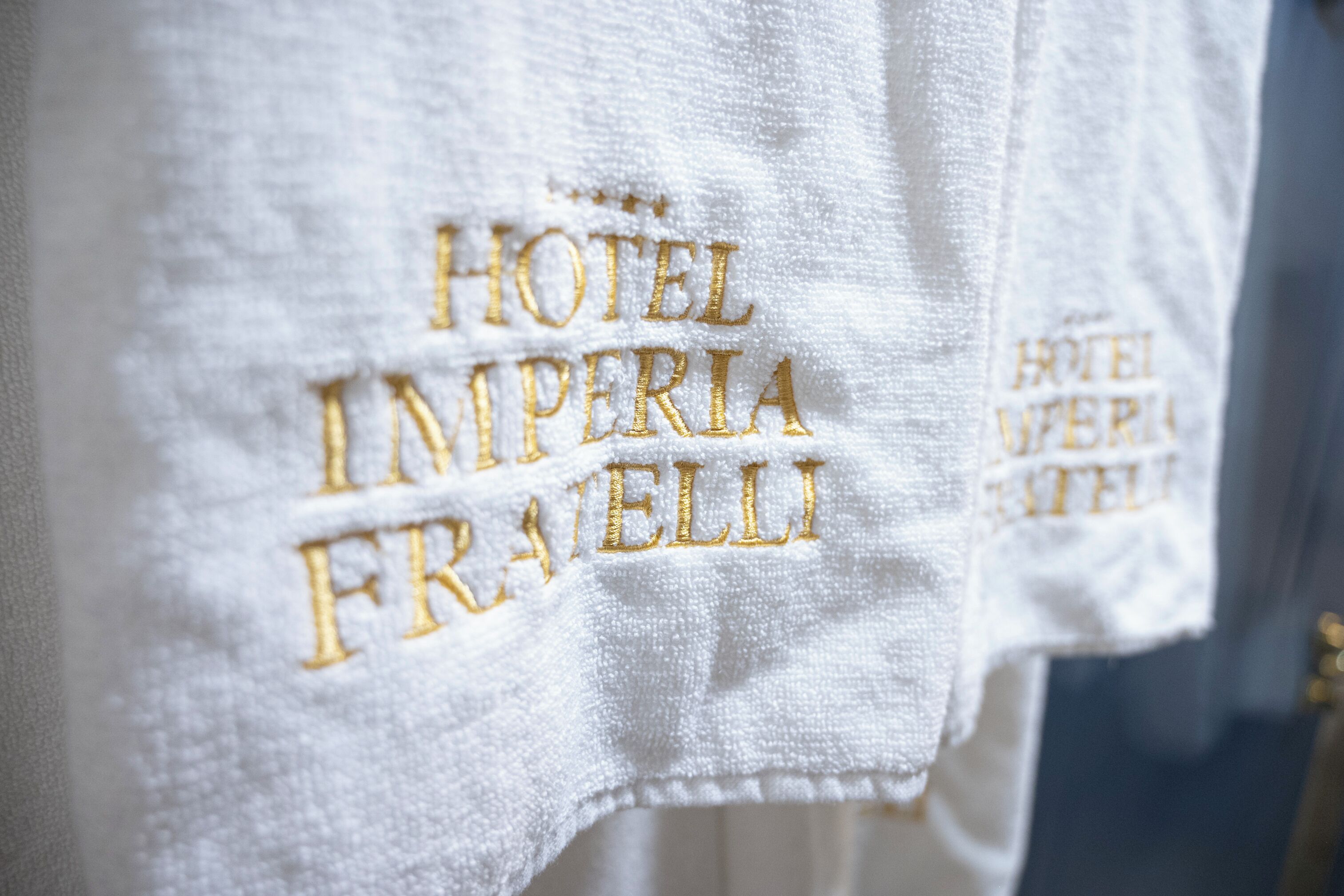Une serviette blanche ornée d’une broderie dorée portant l’inscription « HÔTEL IMPERIA FRANZELLI ».