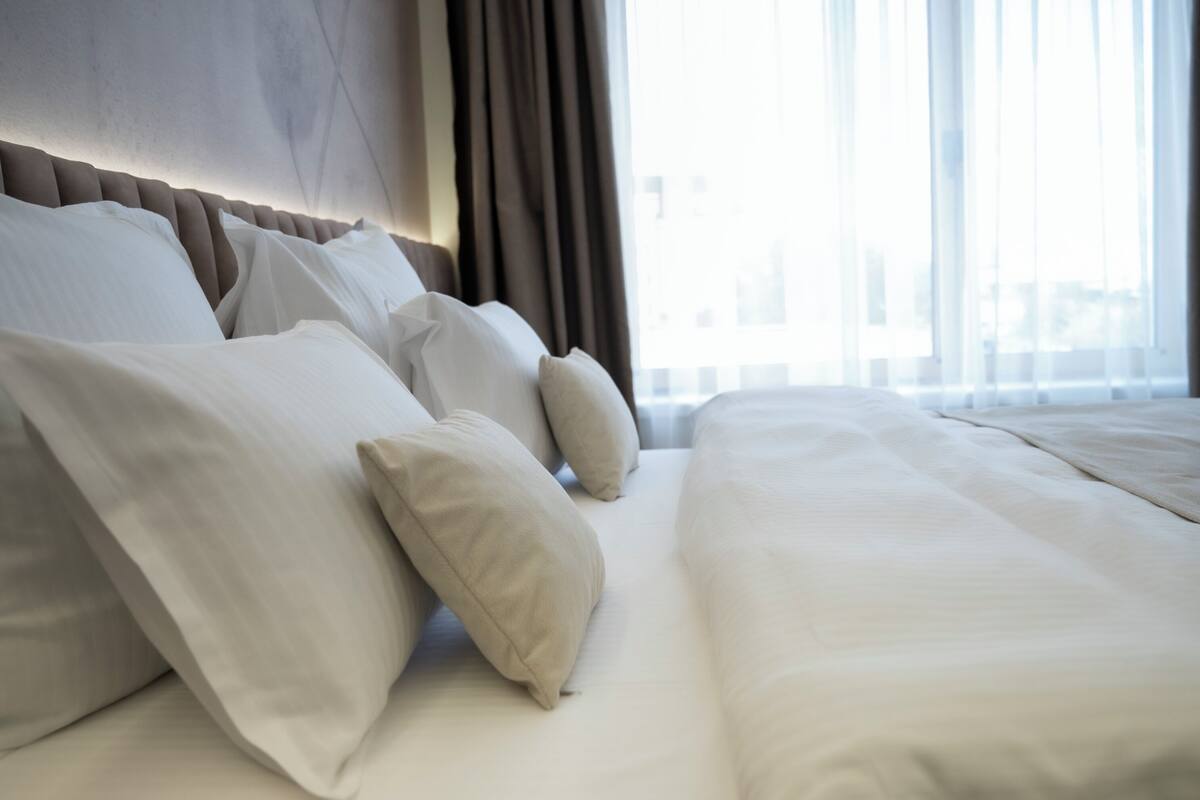 A neatly made bed with pillows, a headboard, and a window with curtains.