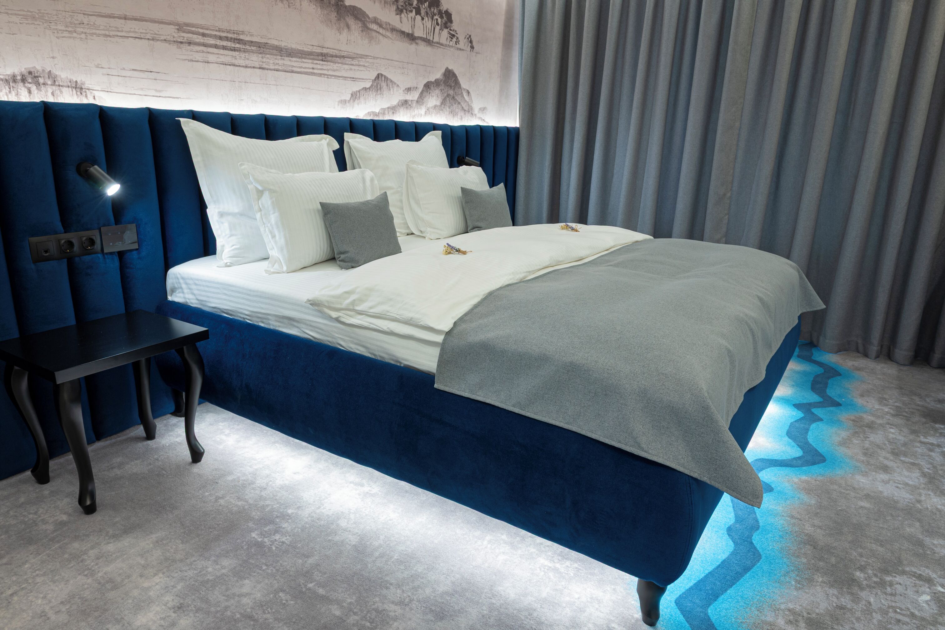 Quarto moderno com uma cama grande, uma mesinha de cabeceira e uma luminária fixada na parede.