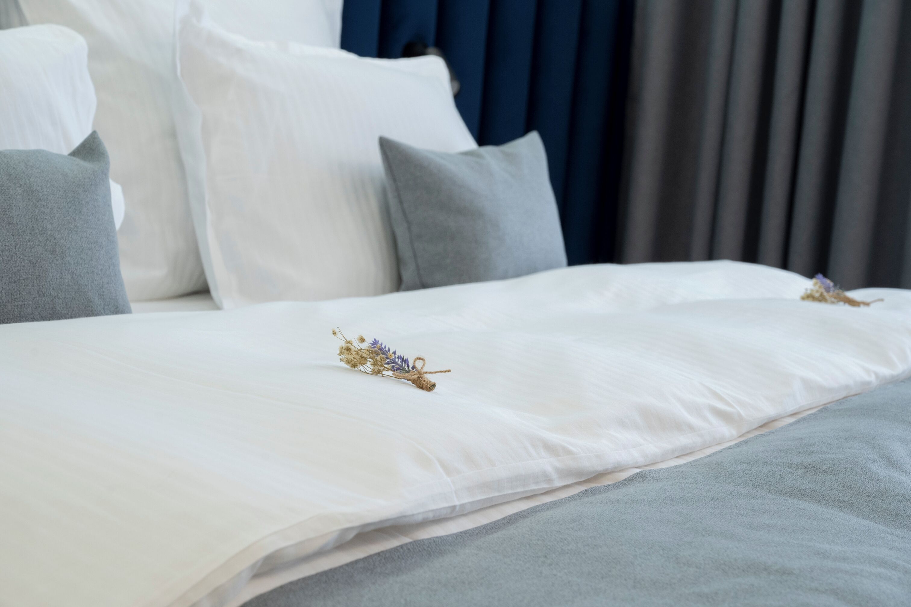 A neatly made bed with white and grey bedding, a decorative floral arrangement, and a dark blue headboard.