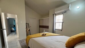 A bedroom with a bed, a bedside table, a mirror, a wardrobe, and a window with blinds. - Charming 2 Bedroom Home in Phoenix Park Village (Portmore)