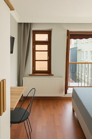 A bedroom with a window, radiator, wooden floor, bed, and a view of buildings. - PeraHomes (İstanbul)