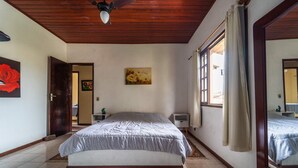 Ein Schlafzimmer mit Bett, Nachttisch, Vorhängen am Fenster und Deckenventilator.