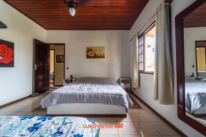 A bedroom with a bed, a bedside table, a nightstand, a window with curtains, and a ceiling fan. - Casa com Piscina e Acesso a Praia em Cabo Frio (Cabo Frio)