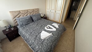 Una cama bien hecha con un edredón estampado, un cabecero y una mesita de noche con una lámpara y una planta pequeña.