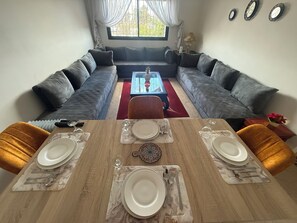 A dining area with a wooden table set for four, two grey sofas facing a glass coffee table, and a window with curtains. - Conveniently located apartment, 2 minutes from Agdal Station   (Rabat)