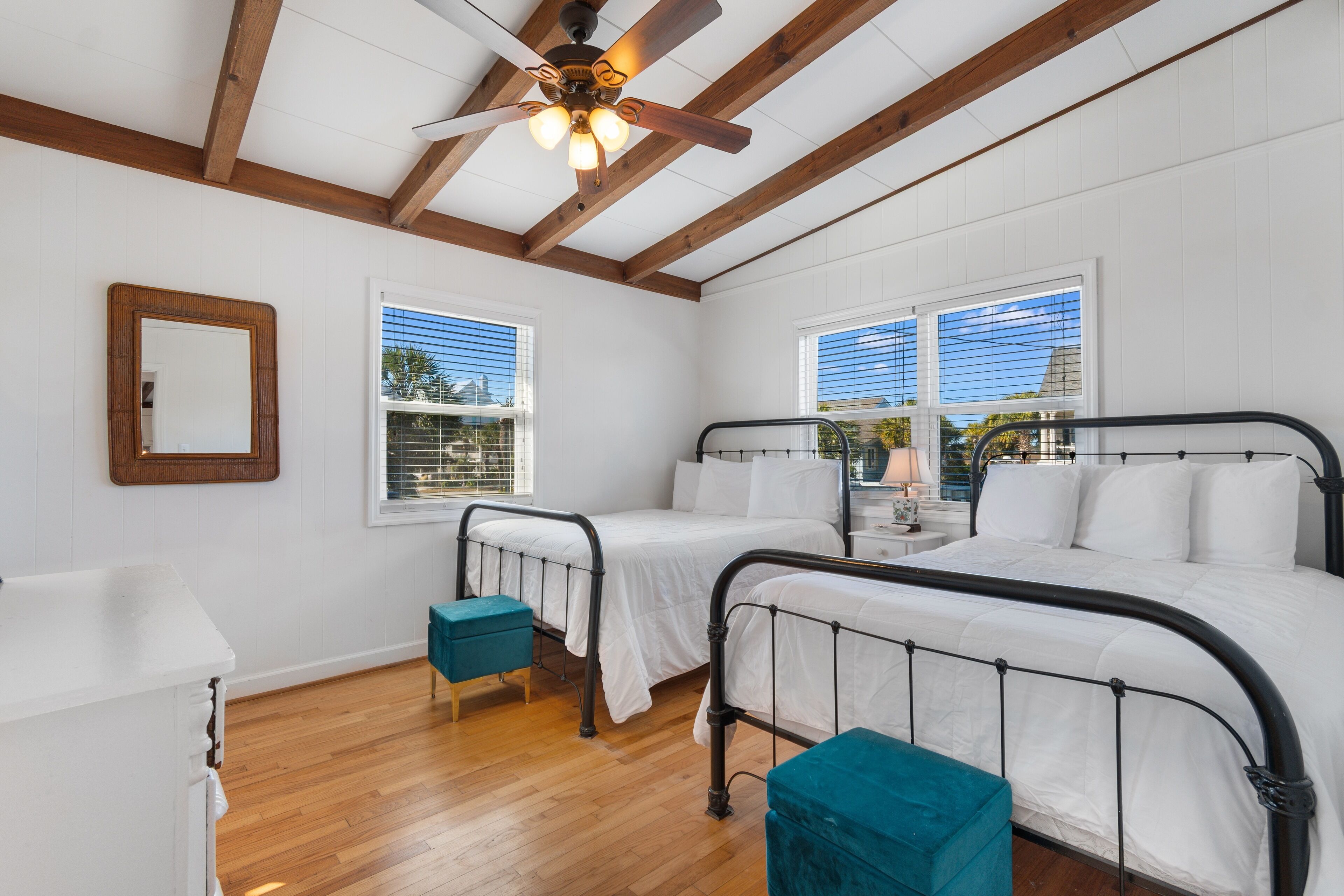 A bedroom with two beds, wooden beams, white walls, and a ceiling fan.