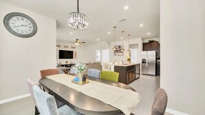 Una cocina moderna con una isla central, un comedor con mesa redonda y una sala de estar con sofá y televisor.