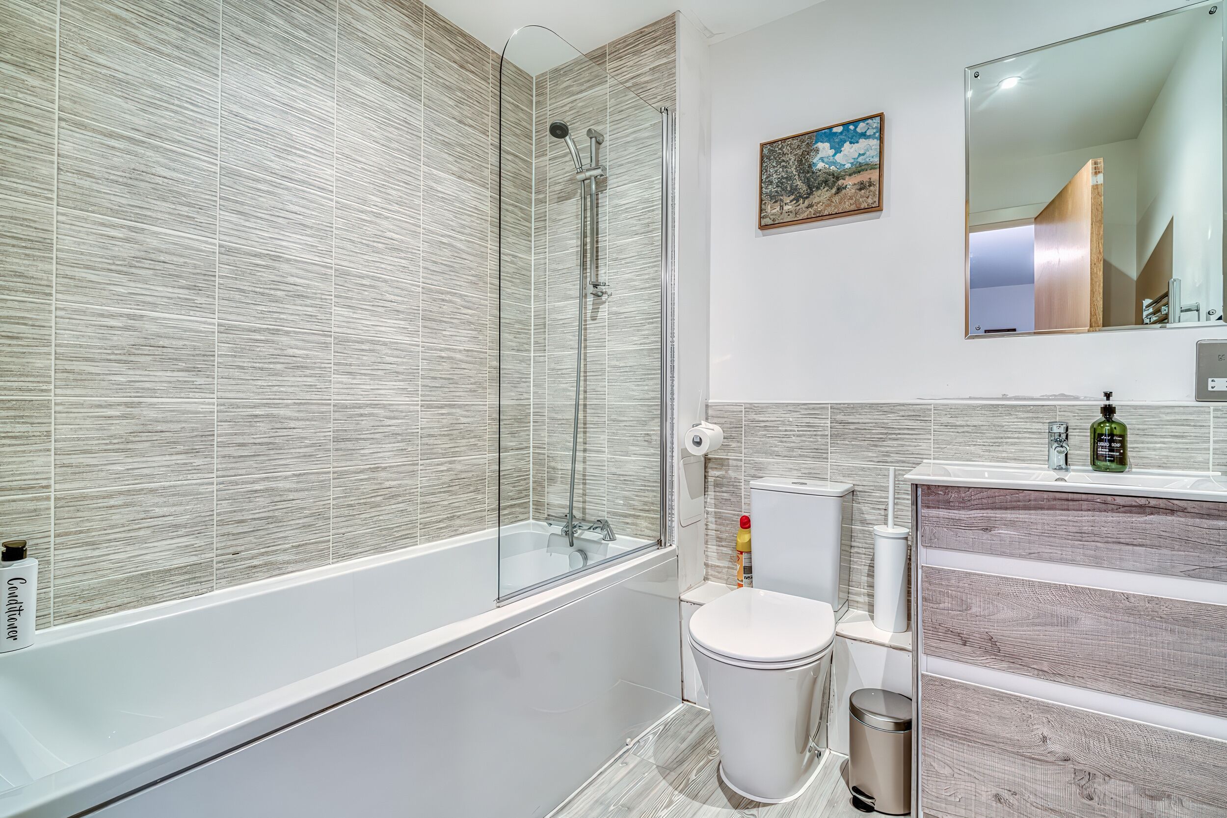 A modern bathroom with a glass-enclosed shower, a white toilet, and a vanity with a mirror.