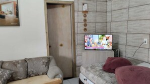 A living room with a sofa, a TV mounted on the wall, and a door. - Pink House Beach and Relaxation (Balneário Arroio do Silva)