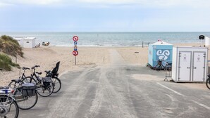Eine Küstenstraße mit abgestellten Fahrrädern, einem Verbotsschild, Strandkörben und einer mobilen Toilette.