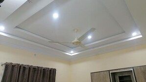 Een kamer met een plafondventilator, inbouwverlichting, een gordijnroede en een kast.