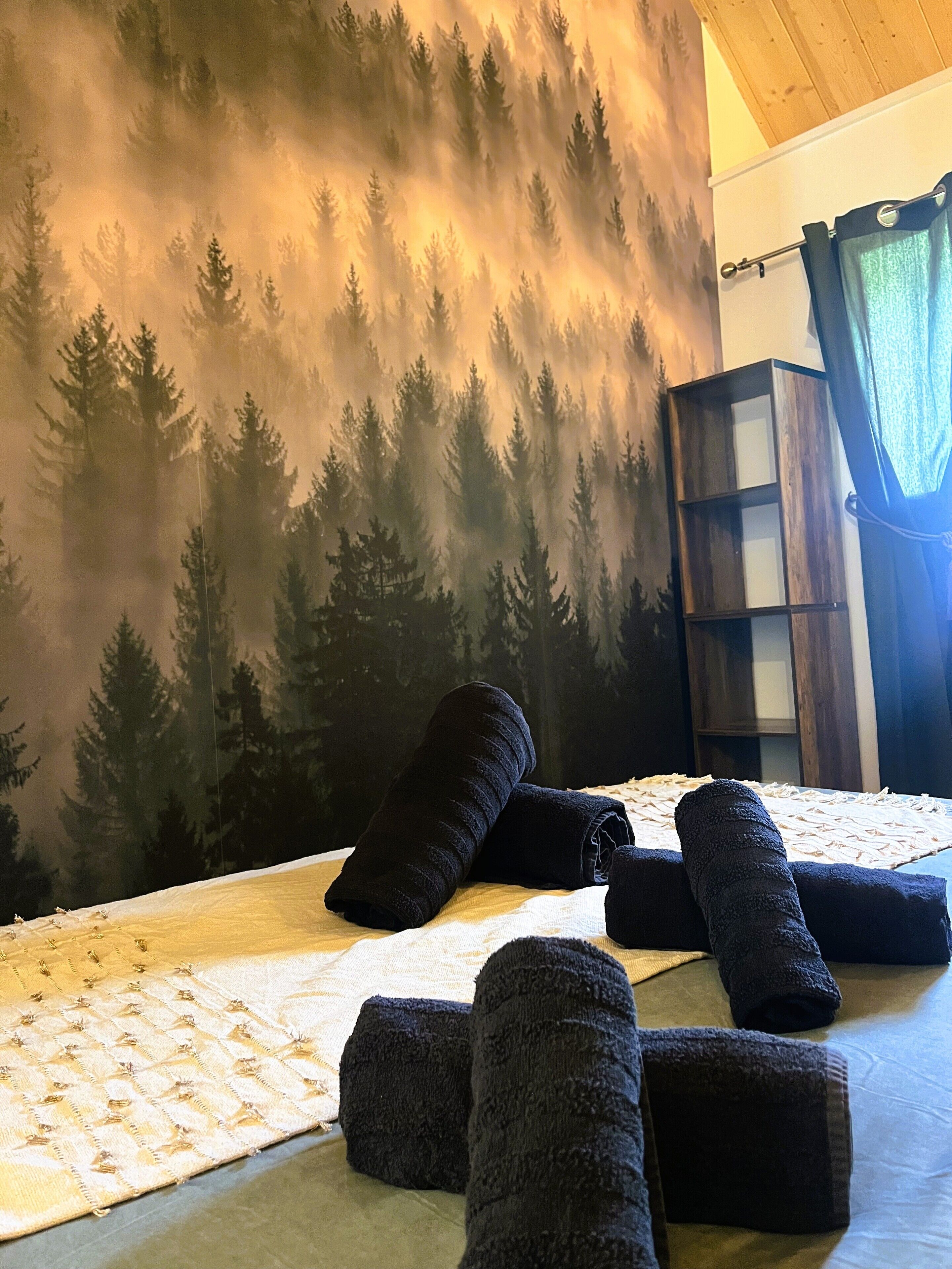 Een kamer met een bed, een muurschildering van bomen, een houten kast en een raam met gordijnen.