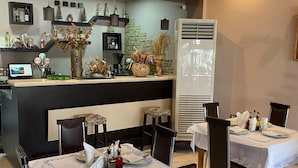 En restaurang med bord som är dukade för middag, en bardisk med olika flaskor och dekorationer samt en modern design med en synlig luftkonditioneringsenhet.
