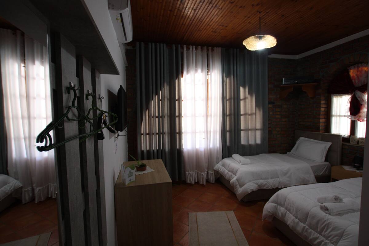 A bedroom with two beds, a wooden desk, and a hanging light fixture.