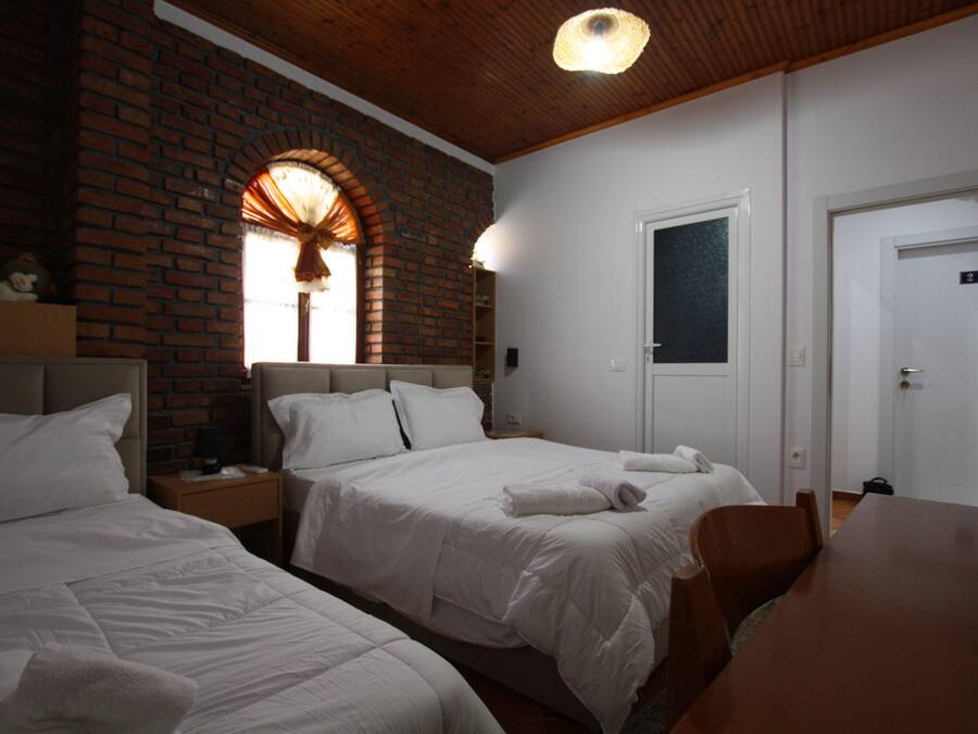 Habitación de hotel con dos camas, una pared de ladrillo, techo de madera y una puerta blanca.