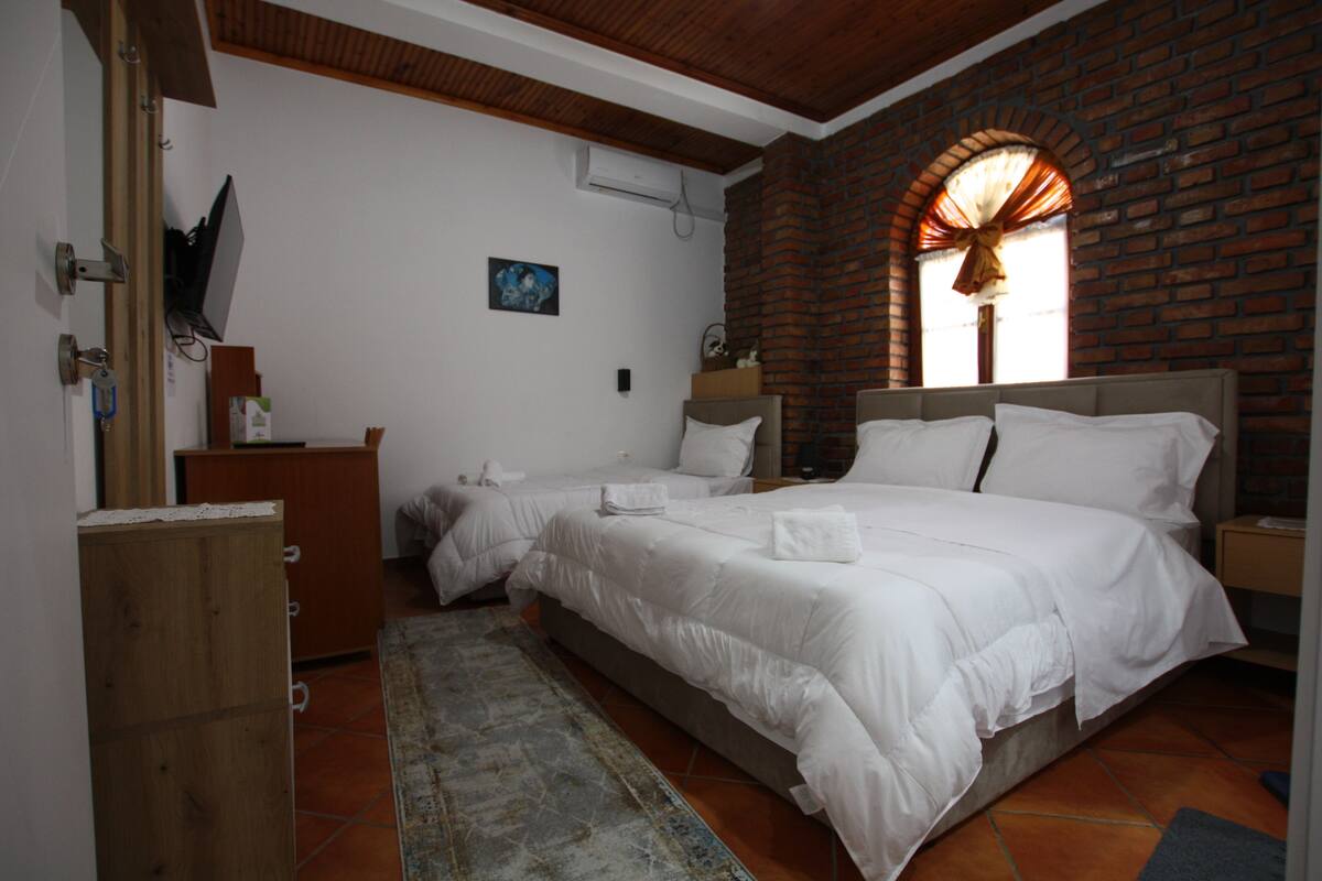 A bedroom with two beds, a wooden dresser, a small table, and a brick wall.