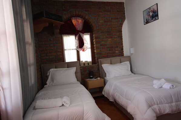Une chambre d’hôtel avec deux lits, un mur en briques, une fenêtre avec un rideau et un tableau accroché au mur.