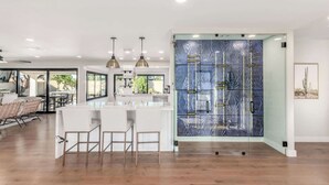 A modern kitchen with a central island, bar stools, pendant lighting, and a large glass partition with a geometric pattern. - NEW |The Pembrook @ Shaw Butte | Pool + Gameroom (Scottsdale)