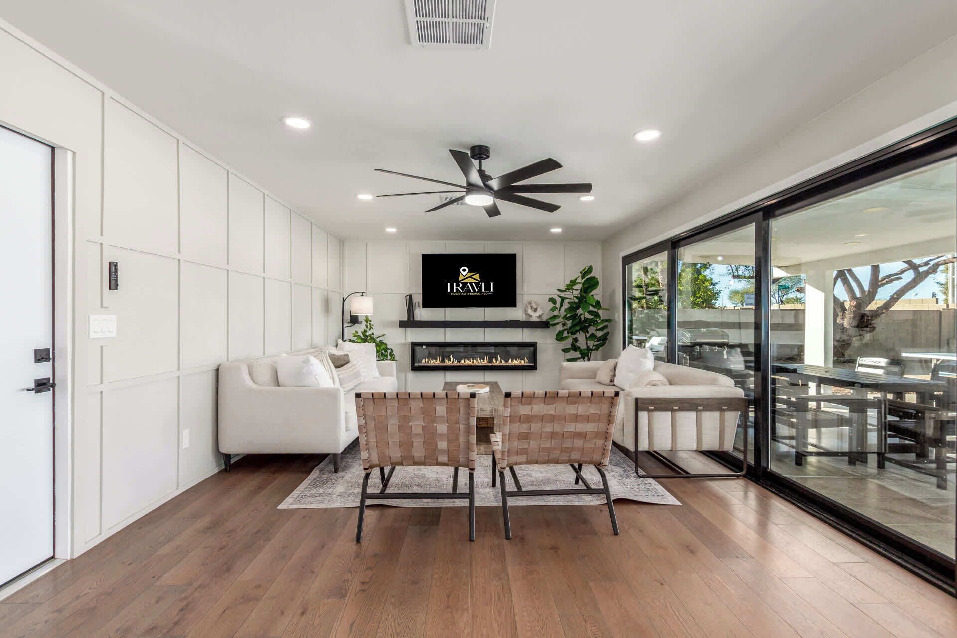 A modern living room with a fireplace, white sofas, a dining area with a glass wall, and a ceiling fan.