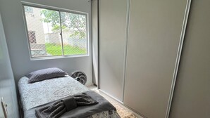 Um quarto com cama, janela, ventilador e porta deslizante.