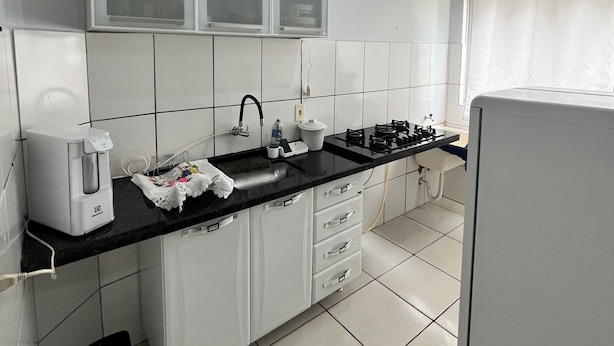 Uma cozinha moderna com armários brancos, bancada preta, cafeteira, pia e fogão.