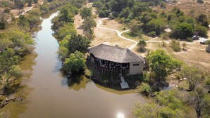 An aerial view of a riverside lodge with a thatched-roof structure, surrounded by dense vegetation and a winding river. - Mozhi Bushcamp  (Kafue National Park)