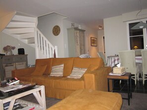 A living room with a sofa, a small table, a bookshelf, a staircase, and a dining area. - Villa "Parfum de dunes", Domaine du golf des Pins, Hardelot, along the golf course. (Neufchâtel-Hardelot)